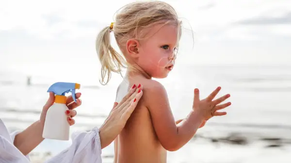 Ochrona przed słońcem jest kluczowa, by uniknąć oparzeń słonecznych u dzieci. Mama smaruje córkę kremem na plaży.