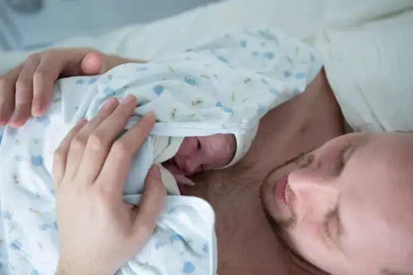 Ciepłe kangurowanie przez tatę po cesarce. Maluszek wtulony w klatkę piersiową ojca, czuje jego bicie serca.